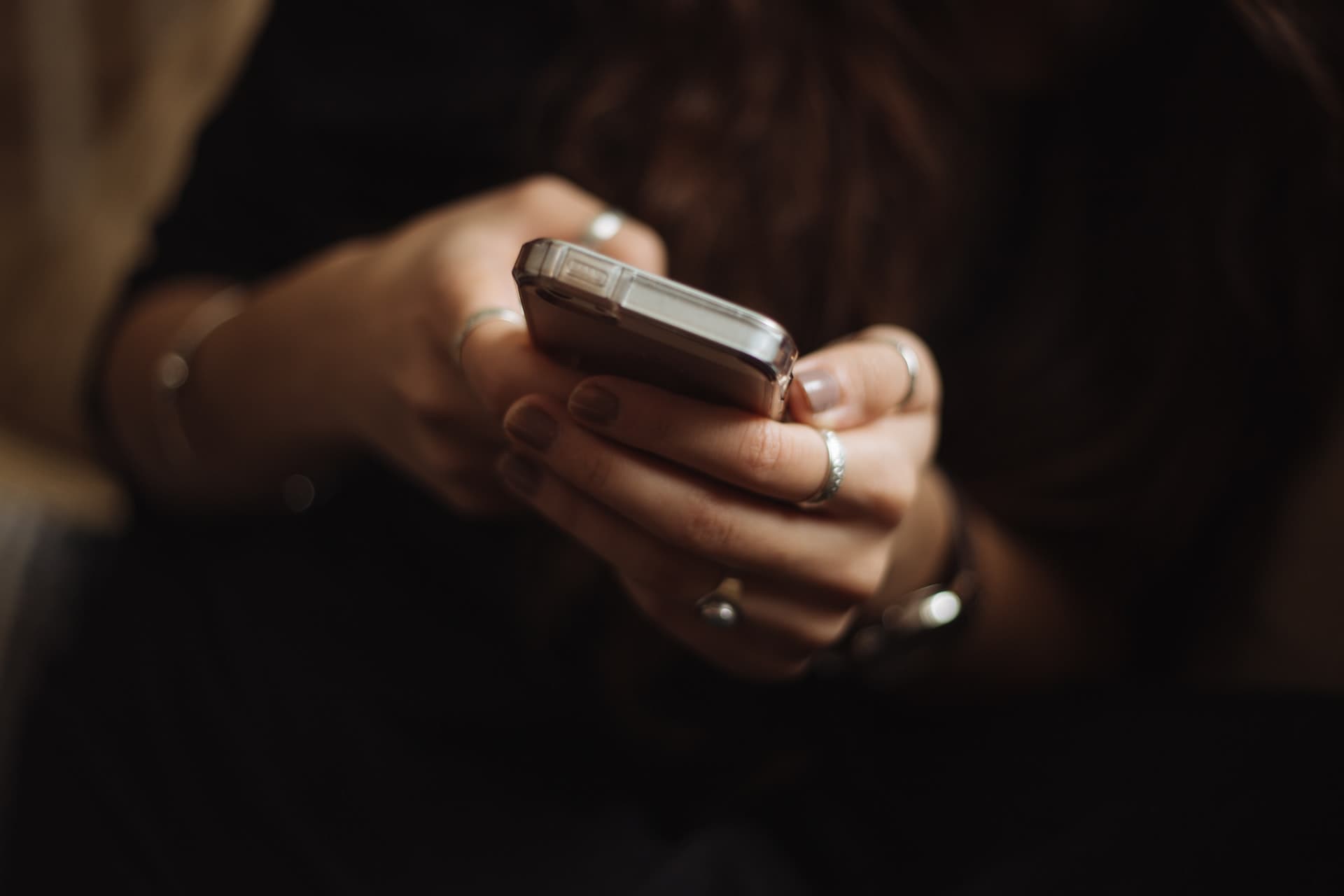 A close-up shot of two hands with rings and painted nails clutching a phone