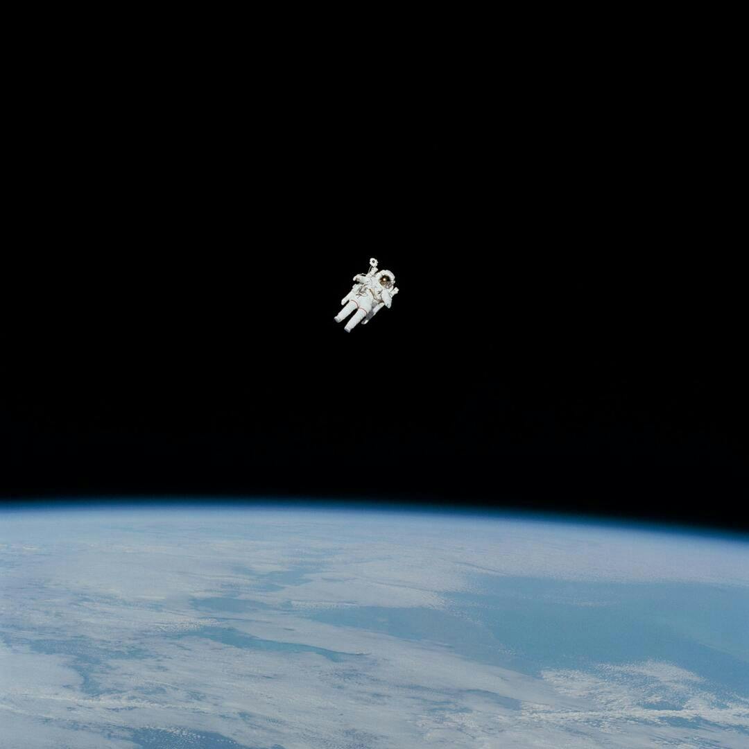 A person in an astronaut suit floats in space above the surface of the Earth