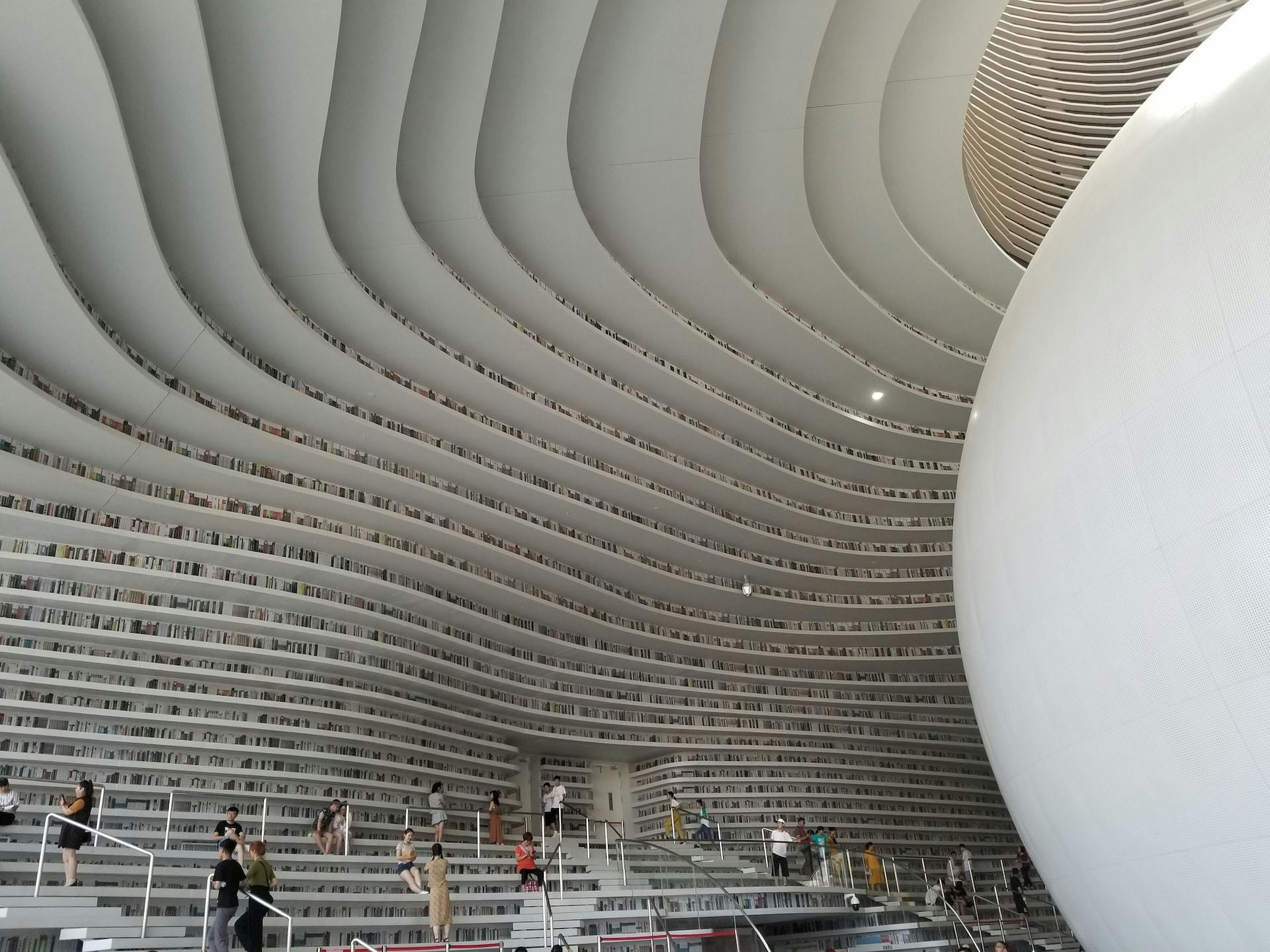 Binhai Library, where patrons stand on some steps while white curved shelves of books extend far above