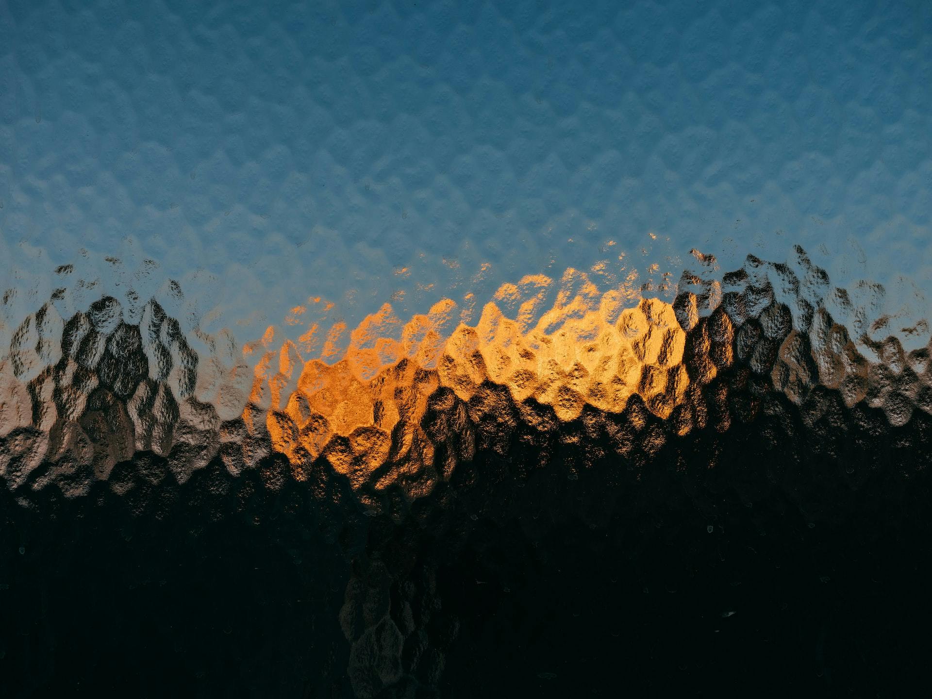 A bumpy reflective surface reflects irregular hexagons of blue, orange, and yellow light