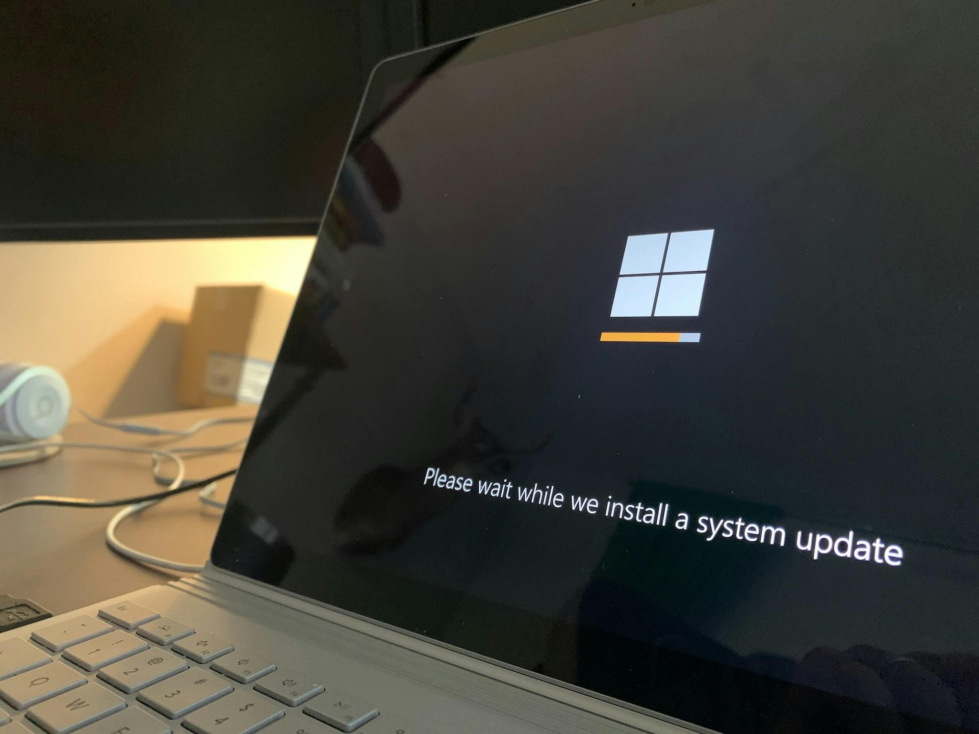 A laptop PC displays the Windows log and the message "Please wait while we install a system update"